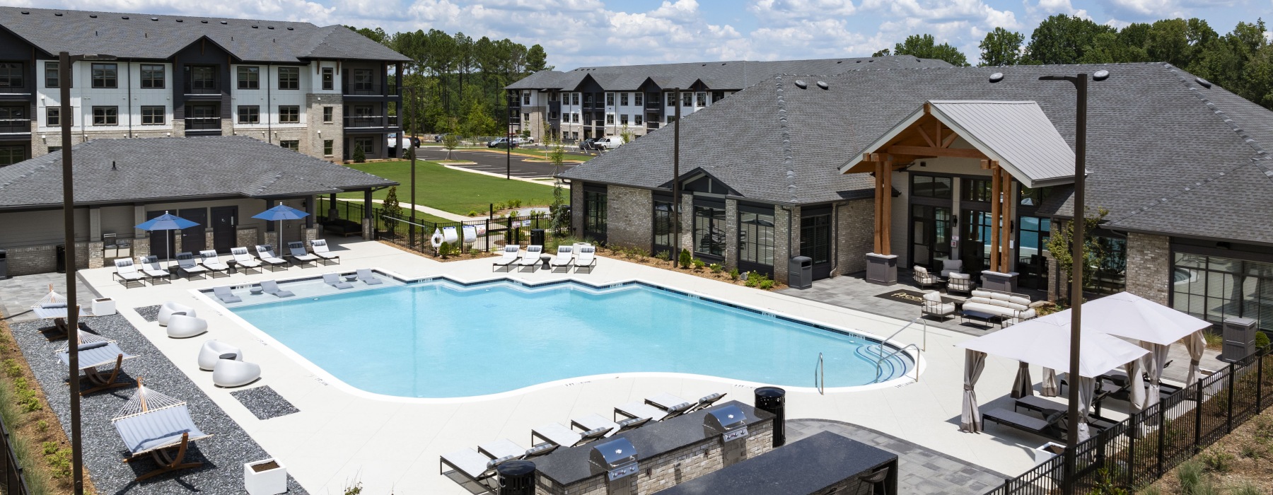 Resort-style swimming pool with lounge chairs and umbrellas in front of poolside lounge at Arcadia at Symphony Park pet-friendly apartments in McDonough